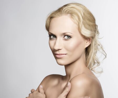 beautiful blonde girl with nudes shoulders and natural makeup, she is turned of three quarters at right with crossed arms, looks in to the lens and smilesの写真素材
