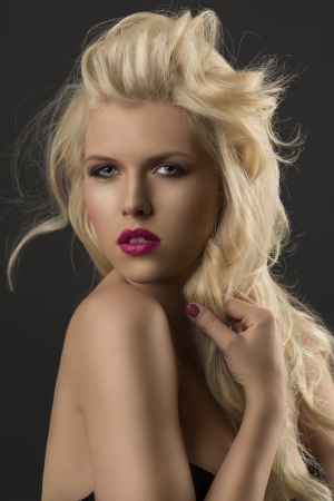 portrait of young sexy girl with blode wavy hairstyle and and flying hair from wind, she looks in to the lens and touches one lock oh hair with right handの写真素材