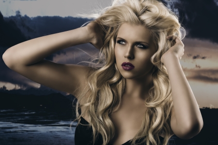 portrait of young sexy girl with blode wavy hairstyle and and flying hair from wind, she is turned of three quarters at right and her hands are on the head in the hairの写真素材