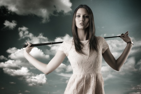 pretty girl with pink elegant dress and golf-club, she is in front of the camera, looks in to the lens and takes the golf-club with both hands on the shouldersの写真素材