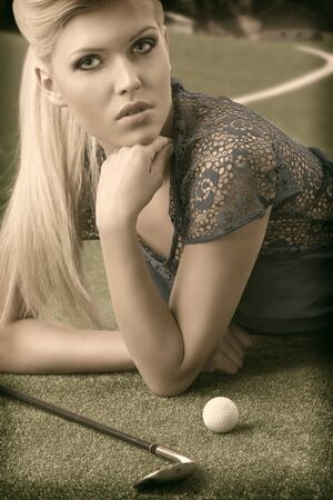 vintage color shot closeup of beautiful blonde girl plays golf with blue dress, lying on the grass near golf-club and ballの写真素材