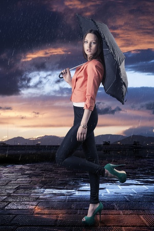 pretty young woman with dark umbrella, her body is turned in profile and she looks in to the lensの写真素材