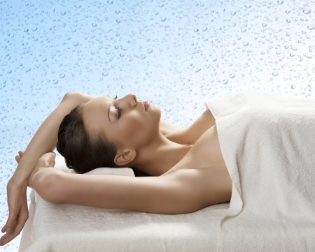 beautiful girl lying on a table with withe towel on her body and under her head, she is in profile with both arms raised behind the headの写真素材