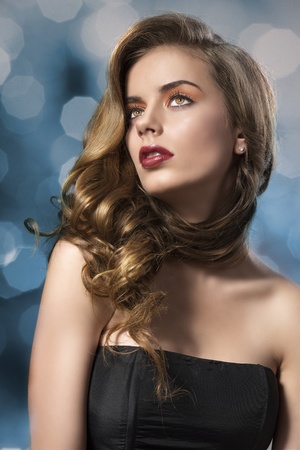 beautiful woman with long wavy hair and dark dress, her face is turned at right and she looks upの写真素材
