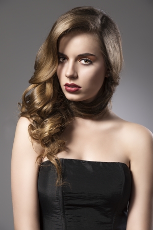 beautiful woman with long wavy hair and dark dress, her face is turned of three quarters at right and looks in to the lensの写真素材