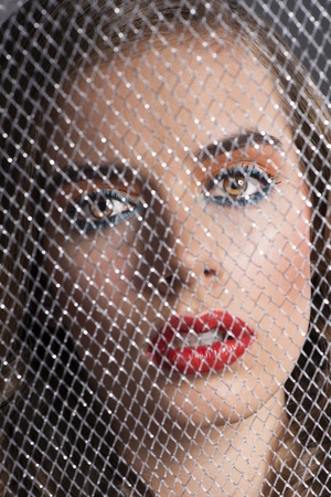 pretty girl with coloured make-up behind grid, she looks in to the lens with serious expressionの写真素材