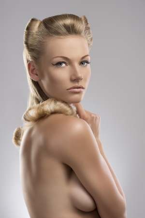 pretty blonde girl with nude torso and creative hair style, she is turned at right and she looks in to the lensの写真素材