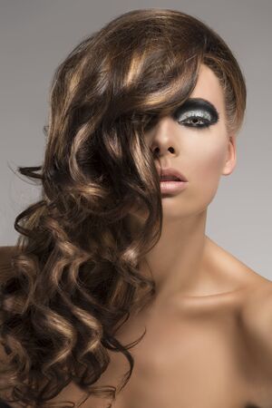 attractive girl with fluffy and wavy hair on the right side, she looks in to the lens with sensual expression and her right side of the face is covered by hairの写真素材