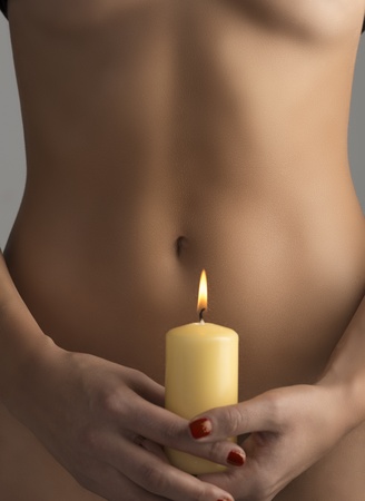 nude belly is behind one yellow candle hold by two hands and fire is near navelの写真素材