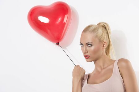 sexy blonde girl with heart shaped balloon, she is turned of three quarters at right and looks in to the lensの写真素材