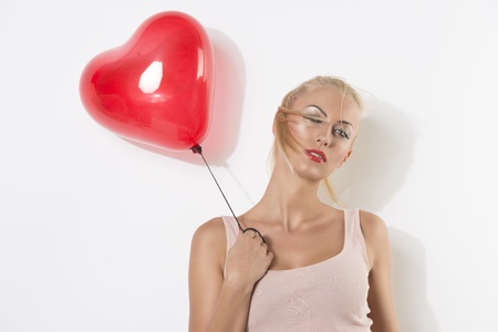 sexy blonde girl with heart shaped balloon, her right hand is near the right shoulder, she looks in to the lens with hair on the faceの写真素材