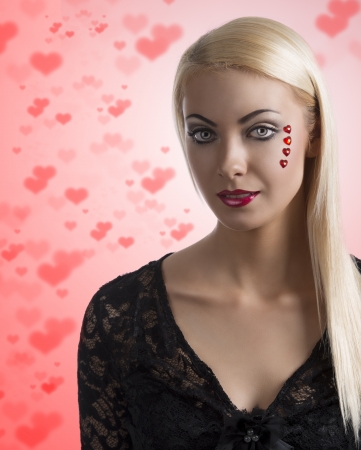 prety blonde girl with sexy clothing and heart shaped decoration on the face, she looks in to the lensの写真素材