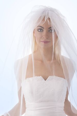 pretty blonde bride with white veil con the face, she is in front of the camera and looks in to the lensの写真素材