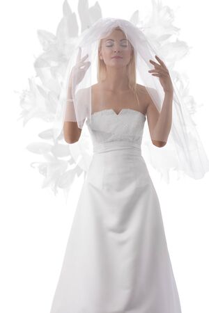 pretty blonde bride with white veil con the face, her hands are under the veil and her eyes are closedの写真素材