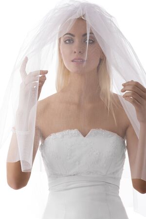 pretty blonde bride with white veil con the face, she looks in to the lens and her hands are under the veilの写真素材