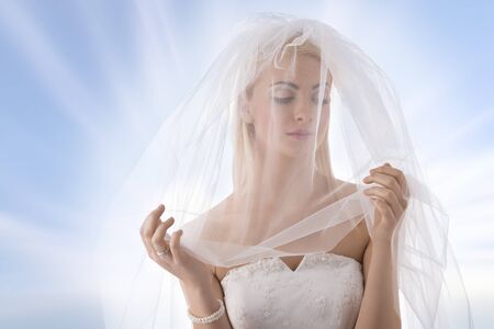pretty blonde bride with white veil con the face, she looks down at leftの写真素材