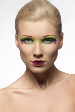 blonde girl with coloured make-up, she is in front of the camera and looks in to the lensの写真素材