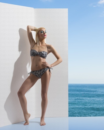 pretty blonde girl with bikini near one white wall, her eyes are closed and her right hand is behind the head and the left hand is on the hipsの写真素材