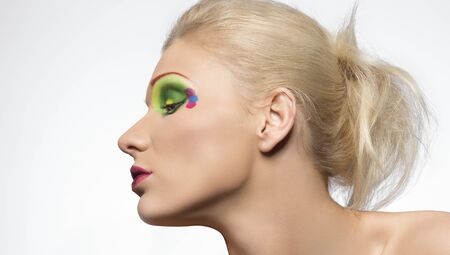 blonde girl with coloured make-up, her face is turned in profile at rightの写真素材