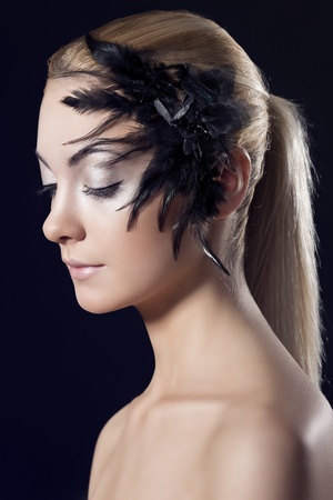 beauty portrait of blonde girl with feathered accessory on the face, she is turned of three quarters and looks downの写真素材