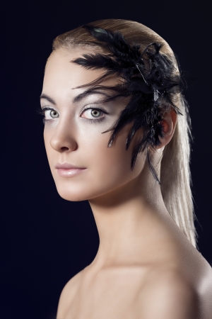 beauty portrait of blonde girl with feathered accessory on the face, she is turned of three quarters and looks in to the lensの写真素材