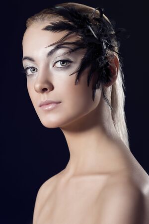 beauty portrait of blonde girl with feathered accessory on the face, she looks in to the lens with serious expressionの写真素材
