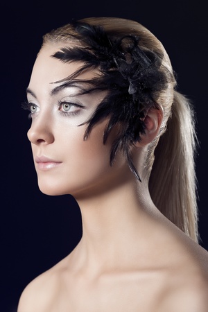 beauty portrait of blonde girl with feathered accessory on the face, she is turned of three quarters at right and looks in front of herの写真素材