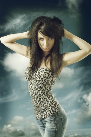 pretty brunette with long hair, blue jeans and leopard t-shirt. She looks in to the lens and had both hands on the headの写真素材