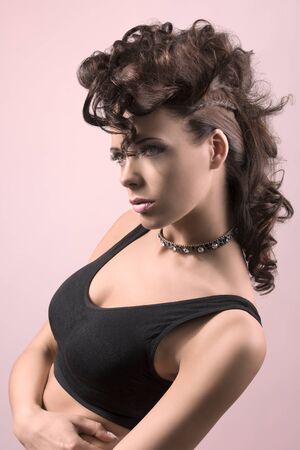 very attractive fashion woman with brown hair and crative hair-style wearing dark top and posing on pink の写真素材
