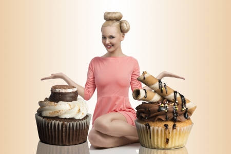 pretty blonde girl with colorful make-up and creative hair-style sitting on the floor and shows two big cupcakesの写真素材
