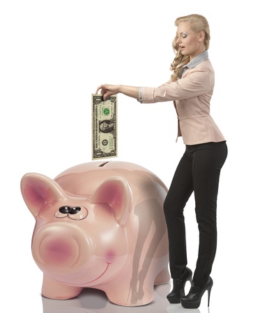 pretty blonde business woman savings one dollar money and putting them in big piggybank. She wearing elegant suitの写真素材