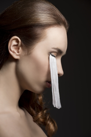 close-up beauty portrait of brunette girl with long eyelashes falling on her face on black backgroundの写真素材