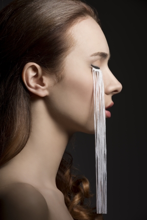 beauty portrait of brunette girl turned in profile with creative make-up and long eyelashes on her face. On black backgroundの写真素材