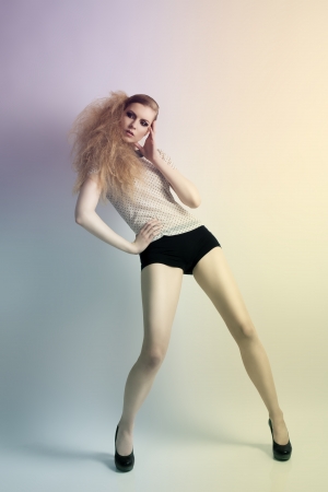 Cute blonde woman with creative hair-style in fashion pose wearing shirt with pois pattern, black shorts and heelsの写真素材