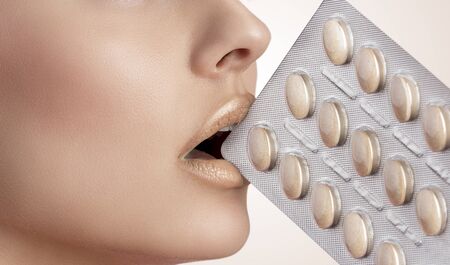 pretty woman with colourful eyeshadow and perfect skin taking blister of pills between her lips. Close-up portrait  の写真素材