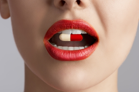 close-up of beauty female mouth with coloured pill between teeth の写真素材