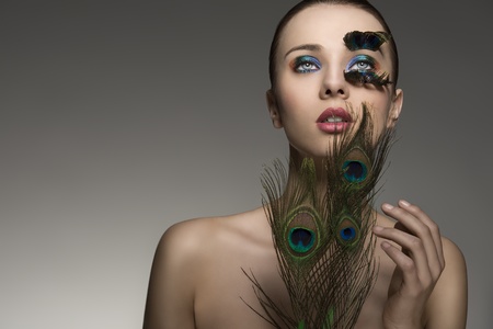 beauty close-up portrait of beautiful brunette lady with naked shoulders and peacock feather in make-up and accessory の写真素材