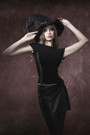 sexy blonde girl with long cute hair and dark make-up posing with gothic clothes and witch hat in Halloween portrait の写真素材
