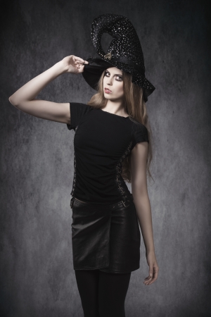 portrait of young blonde female in Halloween day posing with dark style, leather skirt, witch hat and creative make-up の写真素材