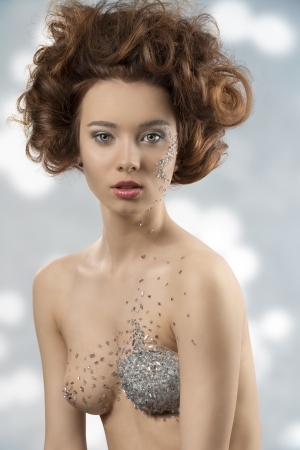 Pretty young girl with fashion hair-style and cute make-up posing with some bright decorations on face and body looking in camera の写真素材