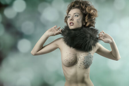 cute brunette girl with elegant hair-style and fur collar posing with her naked body decorated by piece of shiny mirrorsの写真素材