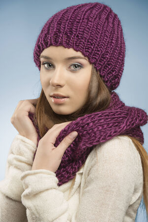 attractive girl with long smooth hair posing with winter clothes, she wearing purple wool hat and scarf and white sweater and looking in camera の写真素材