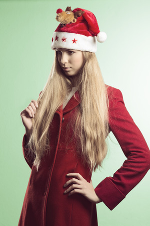 portrait of pretty young girl with long blonde hair, natural make-up and winter clothes. She wearing red coat and funny red santa claus hat の写真素材