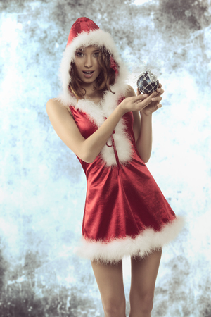 very pretty woman with christmas style wearing short red xmas dress and fur hood. Showing the bauble in her hands with happy expression の写真素材