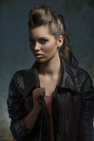 shoot of young fashion girl with wavy brunette hair-style posing with leather jacket in dark atmosphere  の写真素材