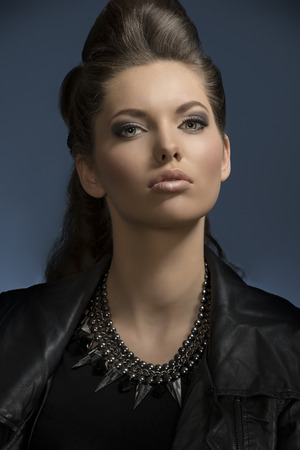pretty girl posing in close-up fashion shoot with dark rock look and cute brown hair-style, wearing leather jacket and modern necklace looking in camera の写真素材