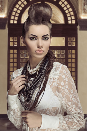 sensual brunette lady posing in fashion portrait with creative hair-style and cute make-up. Wearing sexy white lace shirt and a lot of necklaces の写真素材