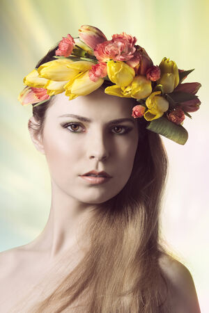 beauty close-up portrait of cute young lady with spring floral style. Looking in camera with colorful make-up and wearing floral spring garland on her head の写真素材