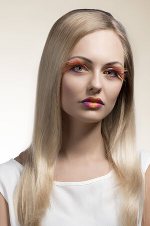 sensual woman with long smooth blonde hair, colorful and creative make-up, feathered eyelashes. Wearing white dress の写真素材