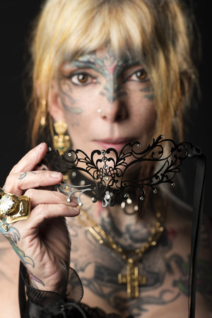Woman , not young , with tattoo on face and arm, ready for party carnival , with black fashion maskの写真素材